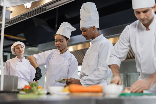 Professional chefs working together in commercial kitchen, preparing food and stirring pan. Culinary teamwork, restaurant industry, hospitality service and food preparation concept.