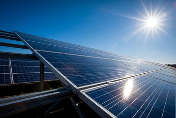 A low angle view of solar panels with a bright sunburst against a clear blue sky