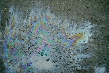Oil spill on asphalt forming colorful iridescent rainbow pattern and showing environmental pollution.