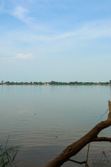 Tranquil wide river flowing peacefully under a clear light blue sky with distant green treeline and calm water ripples, evoking a serene natural landscape.