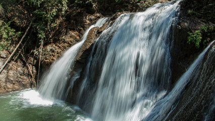 Obraz premium Beautiful waterfall cascading over rocks in lush forest, flowing freshwater in natural tropical landscape, peaceful scenic travel destination.