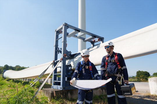 Engineers in safety gear conduct a detailed inspection of wind turbine blades at a construction site. Large blades are placed on the ground, highlighting the renewable energy technology.