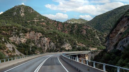 Winding mountain road with asphalt curves leading to a majestic rocky peak under a blue cloudy sky. Beautiful scenic landscape for travel and adventure concepts