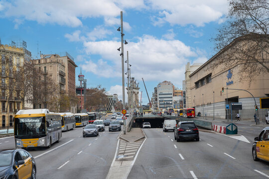 Busy city street with public buses and cars traffic in Barcelona, Spain. Urban transportation infrastructure and architecture under a cloudy blue sky