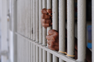 Obraz premium hands of a prisoner behind prison bars on black background