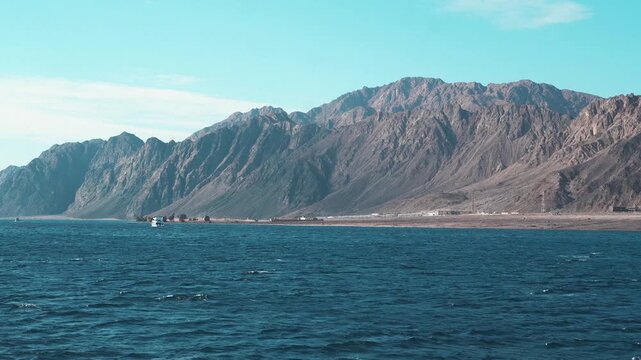 A panoramic summer travel landscape featuring a blue ocean coastline where majestic mountains meet the sea under a cloudy sky on a red sea of the gulf of agaba dahab egypt