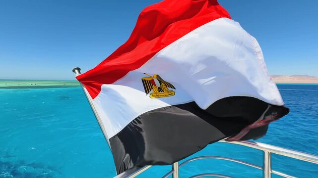 Close up of Egyptian national flag flapping in the strong wind on the upper yacht deck with turquoise sea water in the background