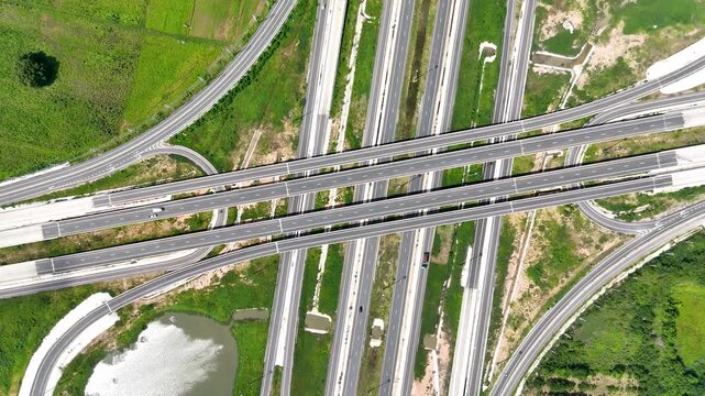 Aerial view of modern highway interchange with multilayer roads and curved ramps surrounded by green farmland, showcasing transportation infrastructure, urban development, and road network planning.