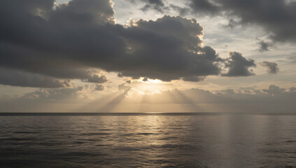 Obraz premium Sky's Embrace: Witness the awe-inspiring dance of sunlight as it filters through the clouds, painting the sea in hues of hope and tranquility. The ethereal beams reach out.