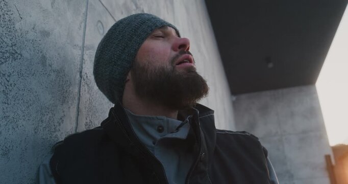After Intensive Shoveling, Worker Catches Breath and Looks Up and Closes Eyes Against Background of Modern Building and Sunset. Exhaustion, Relief, and Human Side of Demanding Winter Upkeep Tasks.