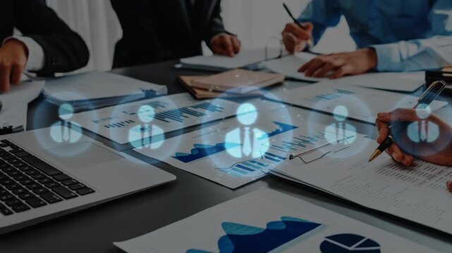 A professional business team collaborates on data analysis using digital icons and charts on a table, highlighting teamwork and strategic planning in a modern workspace. Raster