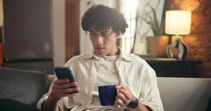 Shocked, coffee and man with phone on couch, news article and negative social media trend for confusion. Upset, headline surprise or person with tea cup in home, mobile app and click bait video intro