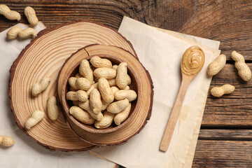 Bowl with unpeeled peanuts and spoon of nut butter on wooden background