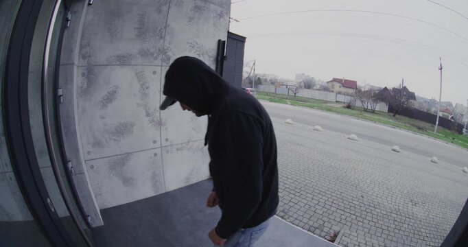 Intruder in Hood Hides Face While Trying to Pick Door Lock. Smart Doorbell Records Criminal Activity at House Entrance, Providing Vital Security Evidence. Security Breach Captured Doorbell Camera.