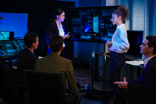 Diverse corporate business team planning global market strategy in late night shift office. Female leader presenting investment project on smart digital screen dashboard.