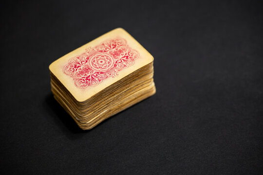 Vintage deck of French playing cards stacked on dark surface. Classic 52 card pack with red back design, worn edges and paper texture, used for Rummy, Joker and casino games.