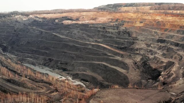 Aerial view of a massive open pit coal mine with stepped terraces and industrial roads, wide panoramic shot of deep quarry excavation site showing environmental impact and mineral extraction