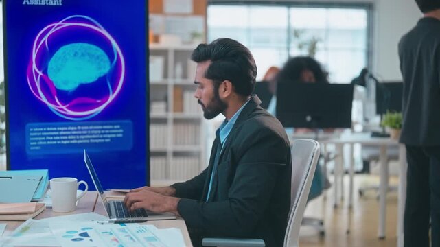 Indian businessman working on laptop in modern office, using smartphone voice recognition and AI assistant technology for communication and productivity.