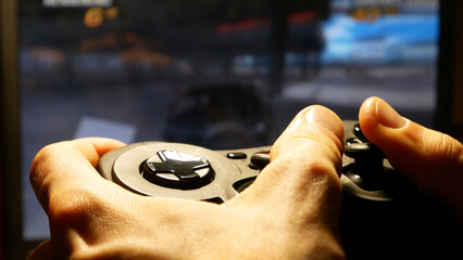Close-up of the hands of a man holding a joystick and playing a computer racing game © Stockah