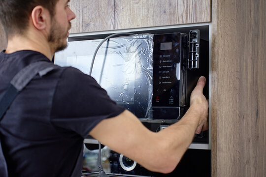 Technician installing new built in microwave into modern kitchen cabinet above oven. Concept of home appliance installation service and household technology using