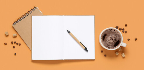 Cup of coffee with beans, notebooks and sugar cubes on orange background