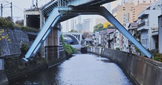 Arches and overpass over canal flowing through Japanese city - wide shot