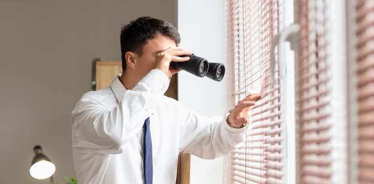 Male FBI agent looking through binoculars near window in office
