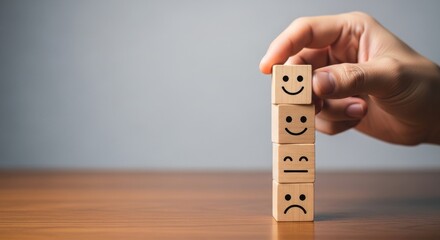 Hand arranges wooden blocks with emotive faces on a wooden table against a blurred background