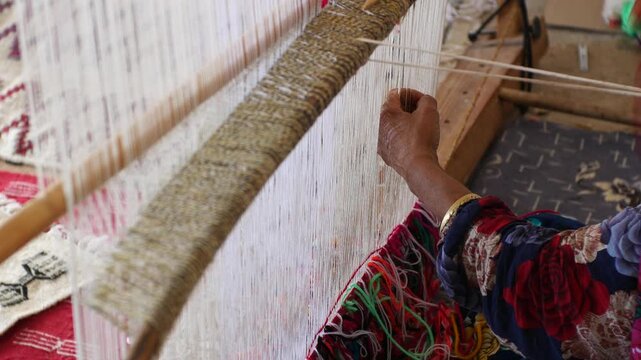 Berber woman weaving traditional carpet on wooden loom, hands tying colorful threads. Close-up of artisan craftsmanship and textile production in Morocco and Tunisie