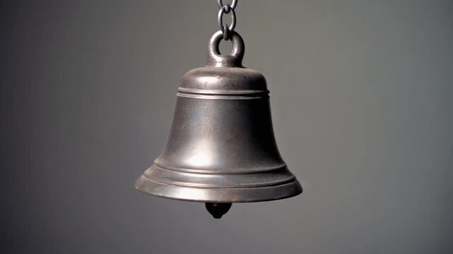 Gracefully swinging antique brass bell suspended by a rustic chain, performing a slow, gentle pendulum motion against a soft, neutral grey background
