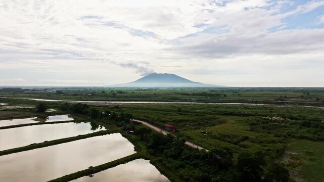 Smooth aerial glide above reflective ponds, green plains, Mount Arayat, Pampanga