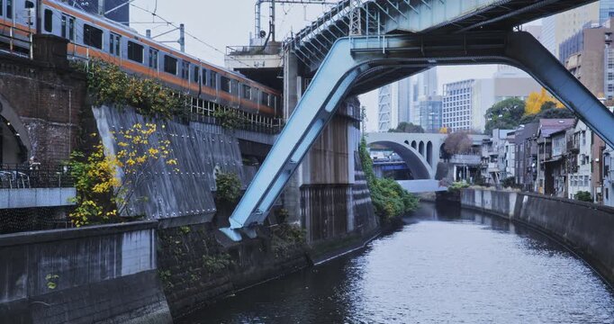 Orange train on hill slowly passing by canal in Japanese city - wide shot