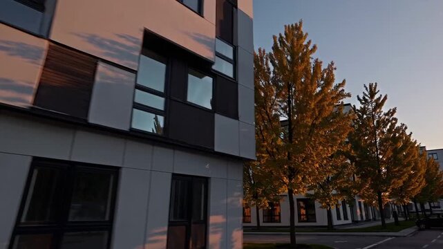 sunset exterior of modern apartment building warm golden light on glass facade and treelined sidewalk quiet street long shadows reflective windows minimalist cladding perfect for architectural