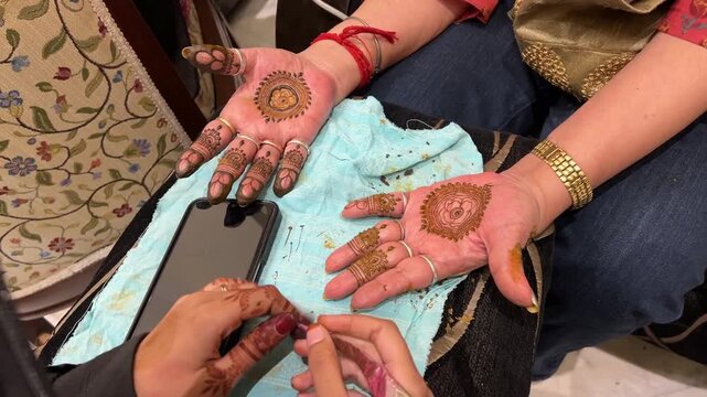 Indian girls wearing mehendi with a design from a smartphone