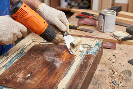 Removing old paint from wooden surface using heat gun and metal scraper tool