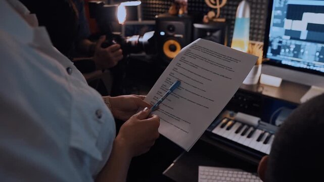Close-up of female hands holding a sheet of paper with notes. Working in a professional music studio with monitors and equalizer on the screen. Music recording studio. Recording the work process of cr