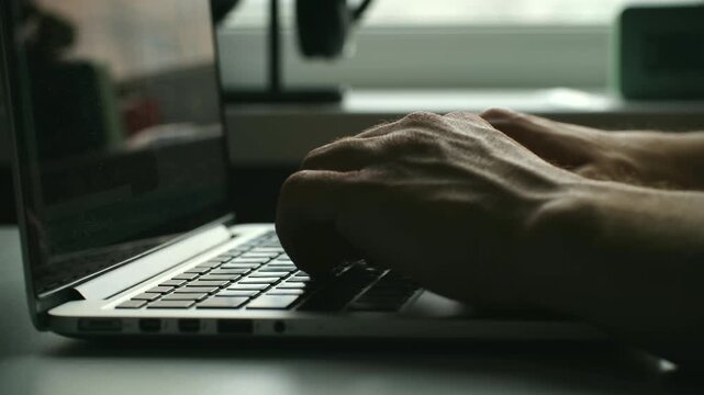 Man hands typing quickly on laptop keyboard. Male programmer, freelancer or office worker working on computer, coding or writing message in dark moody room. Male programmer typing on laptop keyboard