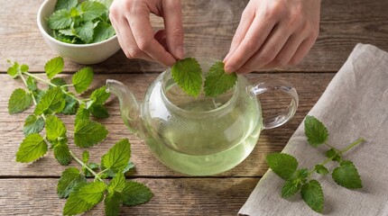 Top Down View of Hands Steeping Fresh Lemon Balm in Glass Teapot with Water Infusing and Turning Pale Green