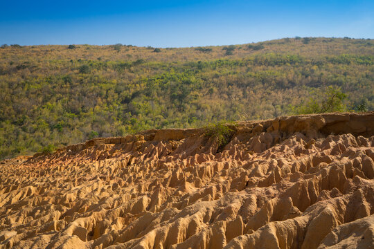 A unique rock landscape featuring deep canyons carved by geological processes, set against a backdrop of mountains and a clear blue sky. This terrain is formed in arid regions through erosion, rainfal