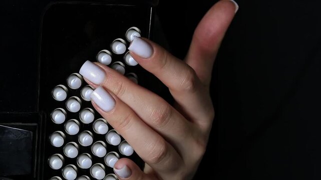 Close up view of female hand with perfect light colored square shape nails pressing white circular buttons on side of black accordion, musician performing music
