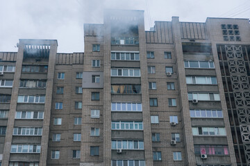 Fototapeta premium A wide shot of a multi-story residential block with smoke rising from the top floors after a major fire. Several windows are broken against a grey winter sky.