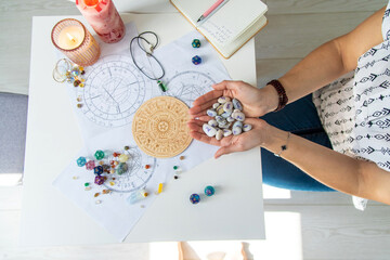 Astrologist hands holding numerology stones over natal charts and zodiac wheel