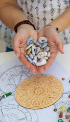 Astrologist hands holding numerology stones over natal charts and zodiac wheel