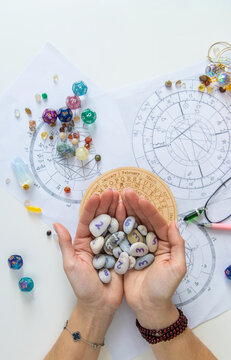 Astrologist hands holding numerology stones over natal charts and zodiac wheel