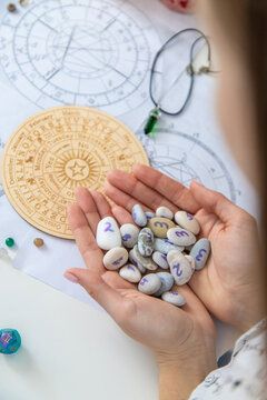 Astrologist hands holding numerology stones over natal charts and zodiac wheel