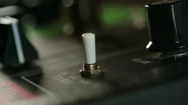 Close up finger flipping white plastic toggle switch on electronic device, turning power on and off to control equipment in dark, moody environment. Person flipping a toggle switch on and off