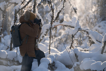 A naturalist photographer in the process of shooting in harsh conditions in a snowy winter forest