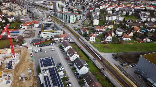 Aerial Drone Footage of Suhr, Aargau, Switzerland &ndash; SBB Trains Passing Through Suburban Landscape with Railway Tracks, Urban Sprawl, and Construction Crane at Dusk