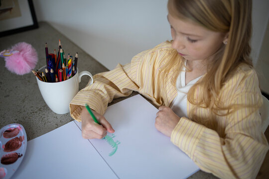 Side View of Young Girl Drawing with a Green Pencil at Home.