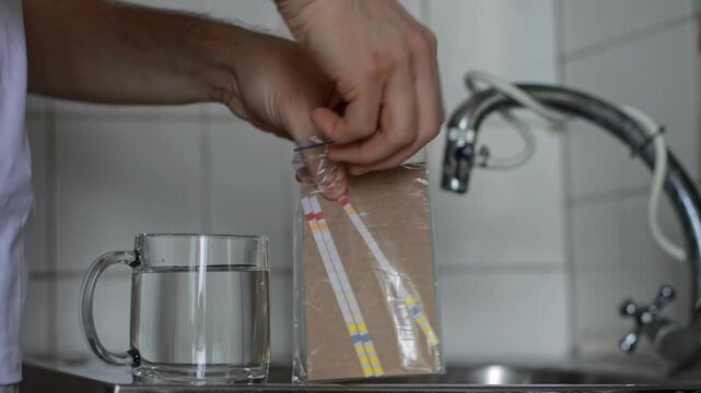 Close-up, male hands removing DIY colored water quality test strip from plastic packaging. Ready to measuring pH level, nitrites, nitrates, hardness, alkalinity, lead, chlorine, cyanuric acid in tap d